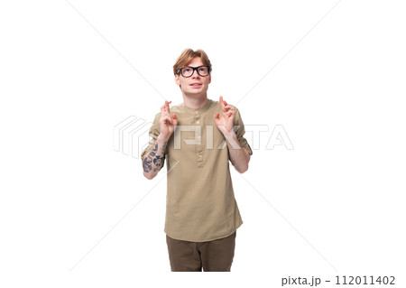 young red-haired caucasian guy dressed in a khaki short-sleeve shirt crossed his fingers and closed young red-haired caucasian guy dressed in a khaki short-sleeve shirt crossed his fingers and closed 112011402
