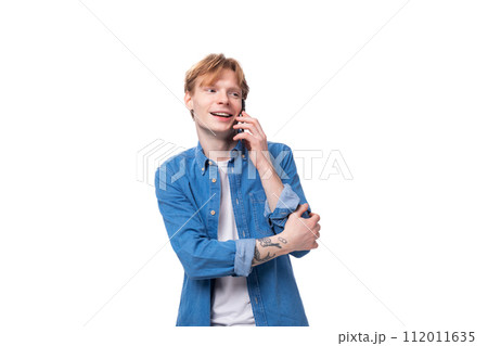 portrait of a smiling caucasian red-haired guy in a denim blue shirt chatting on the phone 112011635