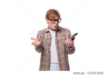 young caucasian red-haired guy in a shirt holding a smartphone at a loss 112011648