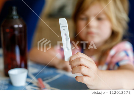 Covid-19 testing children. Sad Child holding self rapid test with positive result. Coronavirus testing. Preschool girl Covid-19 testing children. Sad Child holding self rapid test with positive result. Coronavirus testing. Preschool girl 112012572