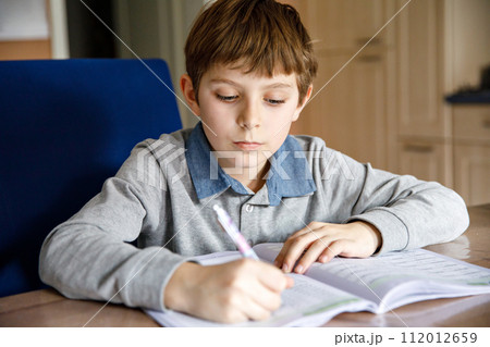 Upset school kid boy making homework during quarantine time from corona pandemic disease. Crying and sad boy frustrating staying at home. Upset school kid boy making homework during quarantine time from corona pandemic disease. Crying and sad boy frustrating staying at home. 112012659