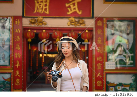Beautiful female traveller with camera standing against a Chinese Temple located in Chang Mai Thailand Beautiful female traveller with camera standing against a Chinese Temple located in Chang Mai Thailand 112012916
