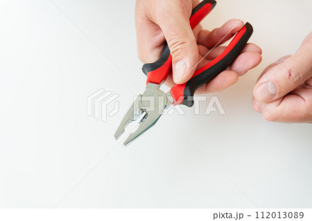 A hand firmly gripping red and black pliers against a white background. A hand firmly gripping red and black pliers against a white background. 112013089