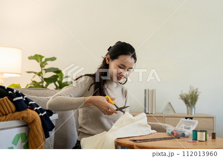 Woman repairs sews reuses fabric from old clothes economical reuse. DIY Hobby Reuse Recycling at home 112013960