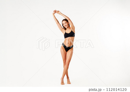 Full length portrait of smiling sporty woman in black underwear posing on white studio background 112014120
