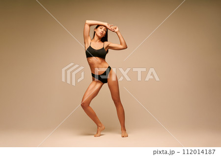 Pretty sporty woman in black underwear posing on beige studio background Pretty sporty woman in black underwear posing on beige studio background 112014187