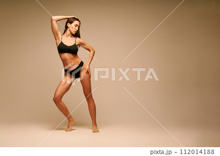 Pretty sporty woman in black underwear posing on beige studio background Pretty sporty woman in black underwear posing on beige studio background 112014188