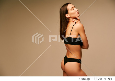 Beautiful sporty woman in black underwear posing on beige studio background 112014194