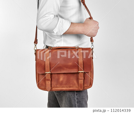 Man carrying copper-colored leather messenger bag over shoulder 112014339