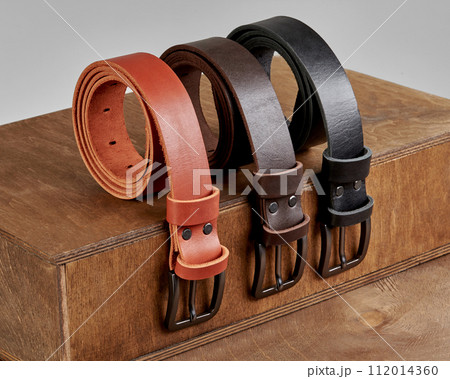 Three rolled leather belts of different colors displayed on wooden podium steps 112014360