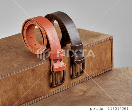 Two leather belts with embossment showcased on wooden display steps 112014361