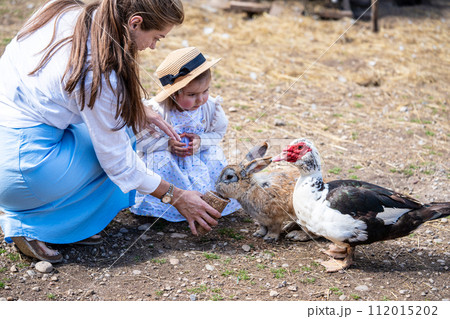 Mom and small daughter feeding rabbits and birds on farm Mom and small daughter feeding rabbits and birds on farm 112015202