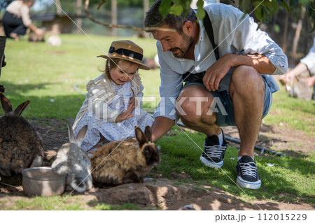 Dad and small daughter feeding rabbits on farm 112015229
