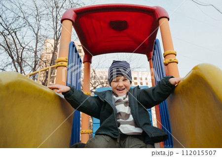 happy smiling child boy rides a slide on playground in autumn 112015507