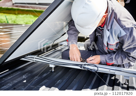 Professional technician securing cables by cable tie. Male worker using special equipment to secure solar cell well. Close up view of man specialist installing solar panel. 112017920