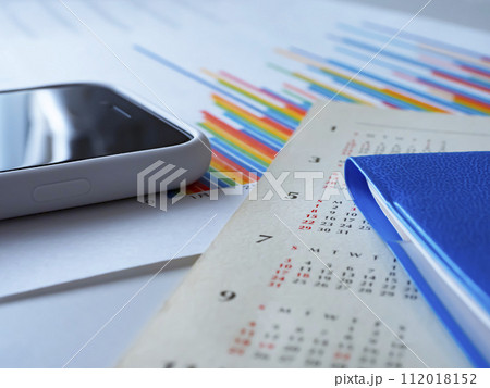 テーブルに置かれたグラフとカレンダーと手帳とスマートフォン 112018152