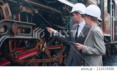 Young caucasian engineer man and woman in suit checking train with tablet in station. 112019986