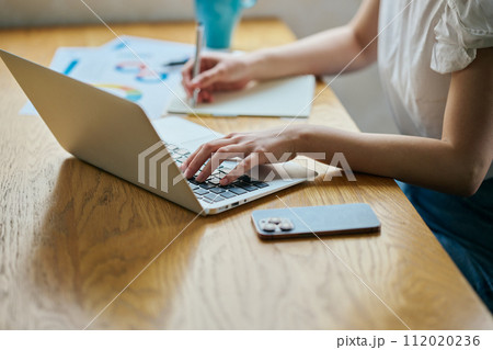 パソコンを操作しながらノートにメモをする若い女性 パソコンを操作しながらノートにメモをする若い女性 112020236