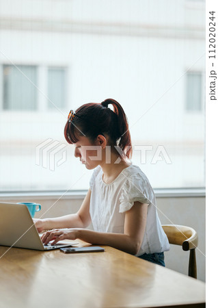 パソコンを操作しながらノートにメモをする若い女性 112020244