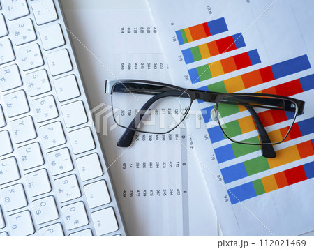 テーブルに置かれたグラフ、書類、キーボード、メガネ テーブルに置かれたグラフ、書類、キーボード、メガネ 112021469