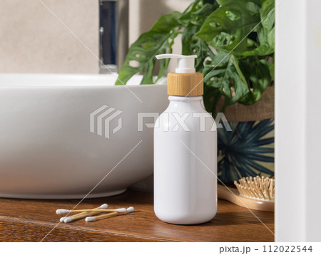 White one pump bottle near basin and green monstera on wooden countertop in bath, mockup White one pump bottle near basin and green monstera on wooden countertop in bath, mockup 112022544