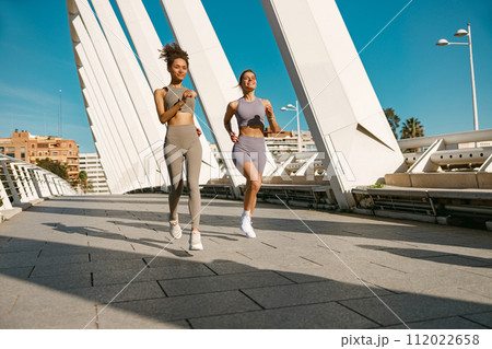 Two active women athlete running side by side along an outdoor track on modern buildings background 112022658