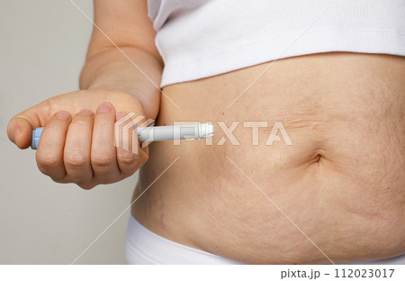Female belly and hand closeup with Semaglutide Injection pen or insulin cartridge pen.  112023017