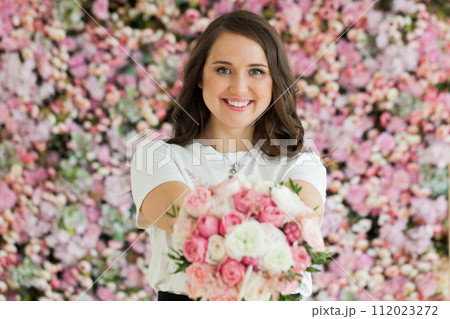 Happy female model taking rose flower standing on blooming floral blossom background.  112023272