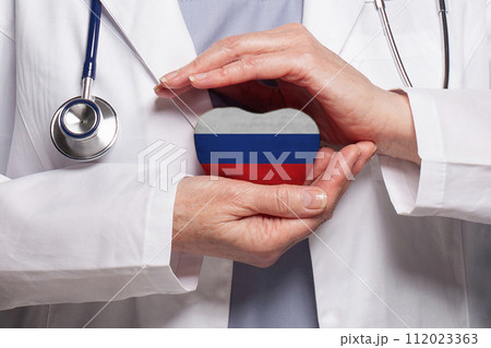 Russian doctor holding heart with flag of Russia background. Healthcare, charity Russian doctor holding heart with flag of Russia background. Healthcare, charity 112023363
