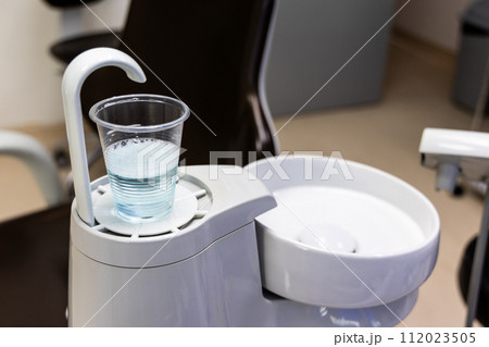 Disposable glass filled with CHX mouth rinse next to spiotoon bowl in dental clinic 112023505