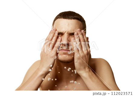 Young brunette man spraying water on his face after shaving against white studio background. Morning routine. Young brunette man spraying water on his face after shaving against white studio background. Morning routine. 112023571