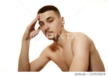 Portrait of bare-chested young male with pensive expression, resting his head on his hand against white studio background. Portrait of bare-chested young male with pensive expression, resting his head on his hand against white studio background. 112023628