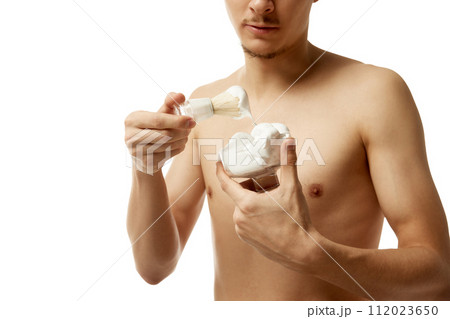 Cropped portrait of man holds container of shaving foam and shaving brush looking at camera against white studio background. Cropped portrait of man holds container of shaving foam and shaving brush looking at camera against white studio background. 112023650