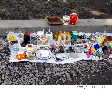 Old dishes, toys and other small items on a blanket on the ground. Flea market, second hand, used items Old dishes, toys and other small items on a blanket on the ground. Flea market, second hand, used items 112024400
