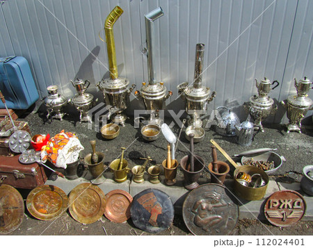 Swap meet. Ancient objects - samovars, mortars, copper plates lie on the ground. Flea market, second hand, used items Swap meet. Ancient objects - samovars, mortars, copper plates lie on the ground. Flea market, second hand, used items 112024401