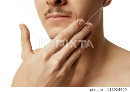 Cropped photo of young man touching his trimmed beard, chin against white studio background. Close-up. 112024496