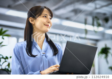 オフィスでノートパソコンを操作するオフィスカジュアルの若い女性 112024910
