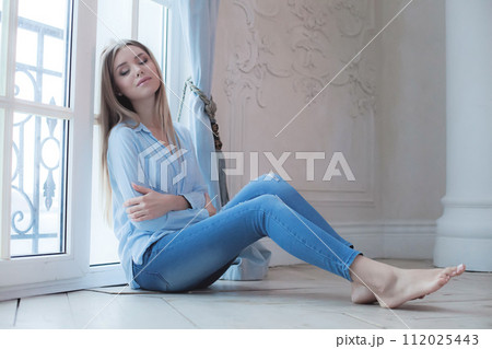 Cheerful young lady relaxing sitting on wooden floor, indoor portrait Cheerful young lady relaxing sitting on wooden floor, indoor portrait 112025443