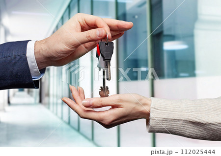 Real estate concept. Estate agent giving house keys against abstract modern office Real estate concept. Estate agent giving house keys against abstract modern office 112025444