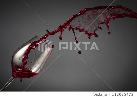 Glass and red wine splash on a dark background. 112025472