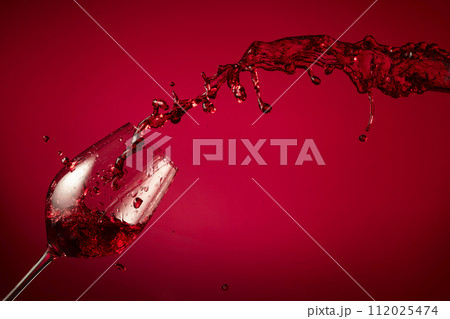 Glass and red wine splash on a red background. Glass and red wine splash on a red background. 112025474