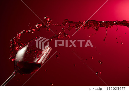 Glass and red wine splash on a dark red background. Glass and red wine splash on a dark red background. 112025475