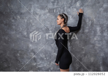 A brunette woman leading a healthy lifestyle performs an exercise to reduce stoop, trains in sports black clothes, leaning with one hand on the wall and placing it behind her back, with copy space A brunette woman leading a healthy lifestyle performs an exercise to reduce stoop, trains in sports black clothes, leaning with one hand on the wall and placing it behind her back, with copy space 112026052