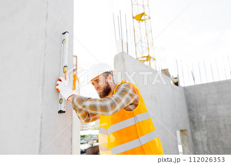 A builder-repairman, foreman, in a protective helmet, checks the evenness of a concrete structure stairs 112026353