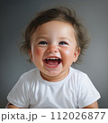 Excited baby boy on a gray background smiling and looking at the camera. Studio shot of an amused small baby with short hair. Cute cheerful child with an open mouth and small white teeth. 112026877