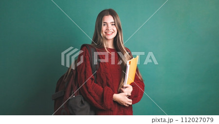 Happy female university student carrying backpack and holding books Happy female university student carrying backpack and holding books 112027079