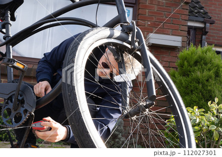 Young man in casual clothes cleaning rust and oiling his city cruiser bicycle chain and gear with spray before riding. Male doing DIY maintenance of his bicycle at home. Selective focus. 112027301