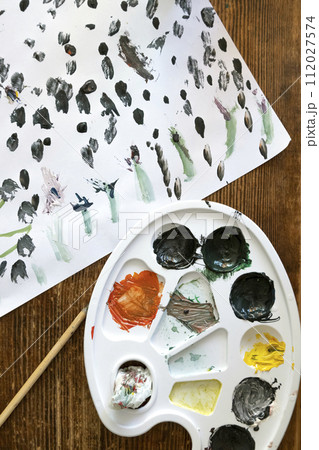A dirty palette for mixing watercolours. On the table - a painted sheet of paper and a brush. The concept of art and hobbies for children. 112027574