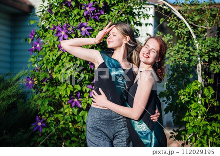 Two girls graduating posing on graduation day. Translation of the inscription: Graduate 2023. 112029195