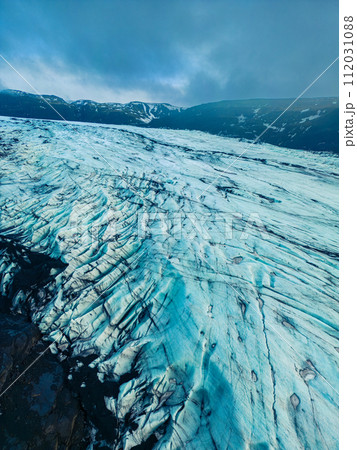 Aerial view of vatnajokull glacier mass in iceland, beautiful ice rocks with massive crevasse around snowy hills and scenery. Majestic frozen icebergs floating on freezing cold lake. Aerial view of vatnajokull glacier mass in iceland, beautiful ice rocks with massive crevasse around snowy hills and scenery. Majestic frozen icebergs floating on freezing cold lake. 112031088